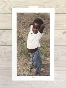 African boy standing outside with his hands behind his head.