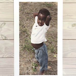 African boy standing outside with his hands behind his head.