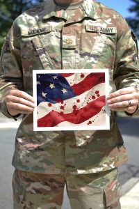 soldier holding art print of American flag with blood splattered on it