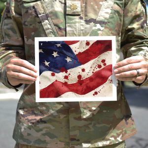 soldier holding art print of American flag with blood splattered on it