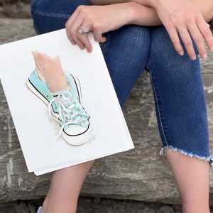 Girl holding watercolor art print of dancing feet wearing Converse sneakers