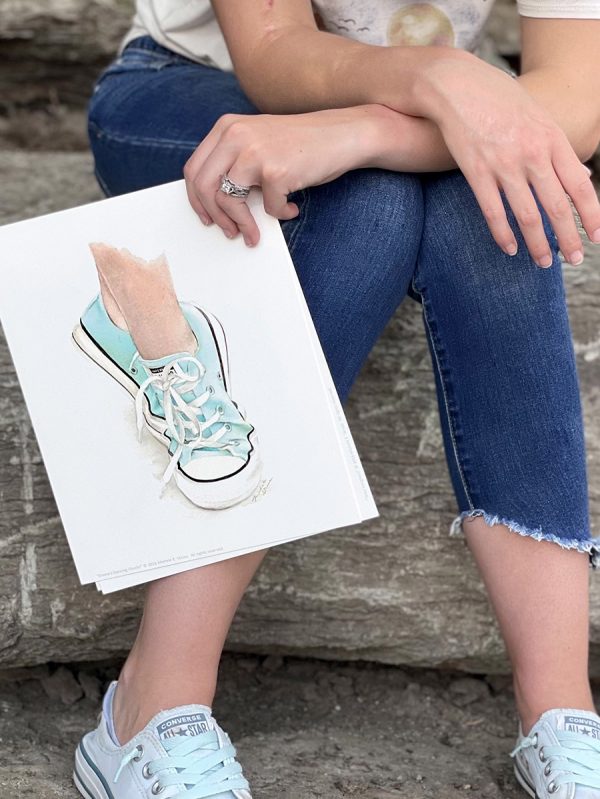 Girl holding watercolor art print of dancing feet wearing Converse sneakers